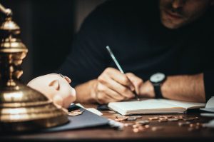 Man writing on a notebook with a piggybank and coins on the table - Financial Planner Image