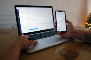 A Person’s Hand in a Laptop and One Hand Holding a Smartphone With Statistics - Mitigate Risk in Investment - Wealth Connexion Blog Image