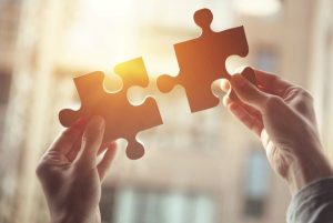 A Man Holding Two Puzzle in a Sunset - Merge Finances With Your Partner - Wealth Connexion Blog Image