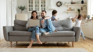 A Couple on a Sofa Looking at the Laptop With Their Kids on the Background - Smart Strategies for Paying Down Debt - Wealth Connexion Blog Image