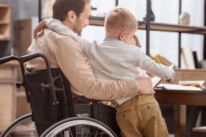 A Man in a Wheelchair Reading a Book to a Child - Difference Insurance Can Make - Wealth Connexion Blog Image