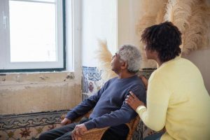 A woman assisting an elder man in a chair looking at the window - Wealth Connexion Blog Image