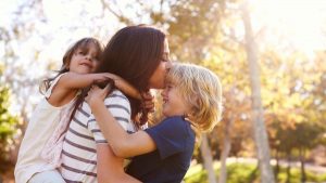 A mother kissing her son on the forehead while carrying her daughter on her back - Wealth Connexion blog image