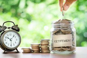Hand putting Coins in glass jar with retro alarm clock for time to money saving for retirement - wealth connexion blog image
