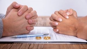 Two hands of two people with a marriage contract, pen, and wedding rings on the table - Wealth Connexion blog image