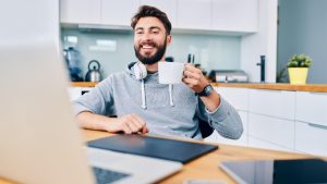 A person holding a coffee cup and wearing headphones while looking in front of a laptop computer - Wealth Connexion blog image
