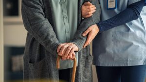 An elderly on a wooden cane assisted by a nurse | Wealth Connexion blog image