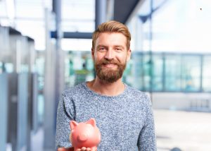 Bearded man in a blue shirt holding a piggy bank - Wealth Connexion blog image